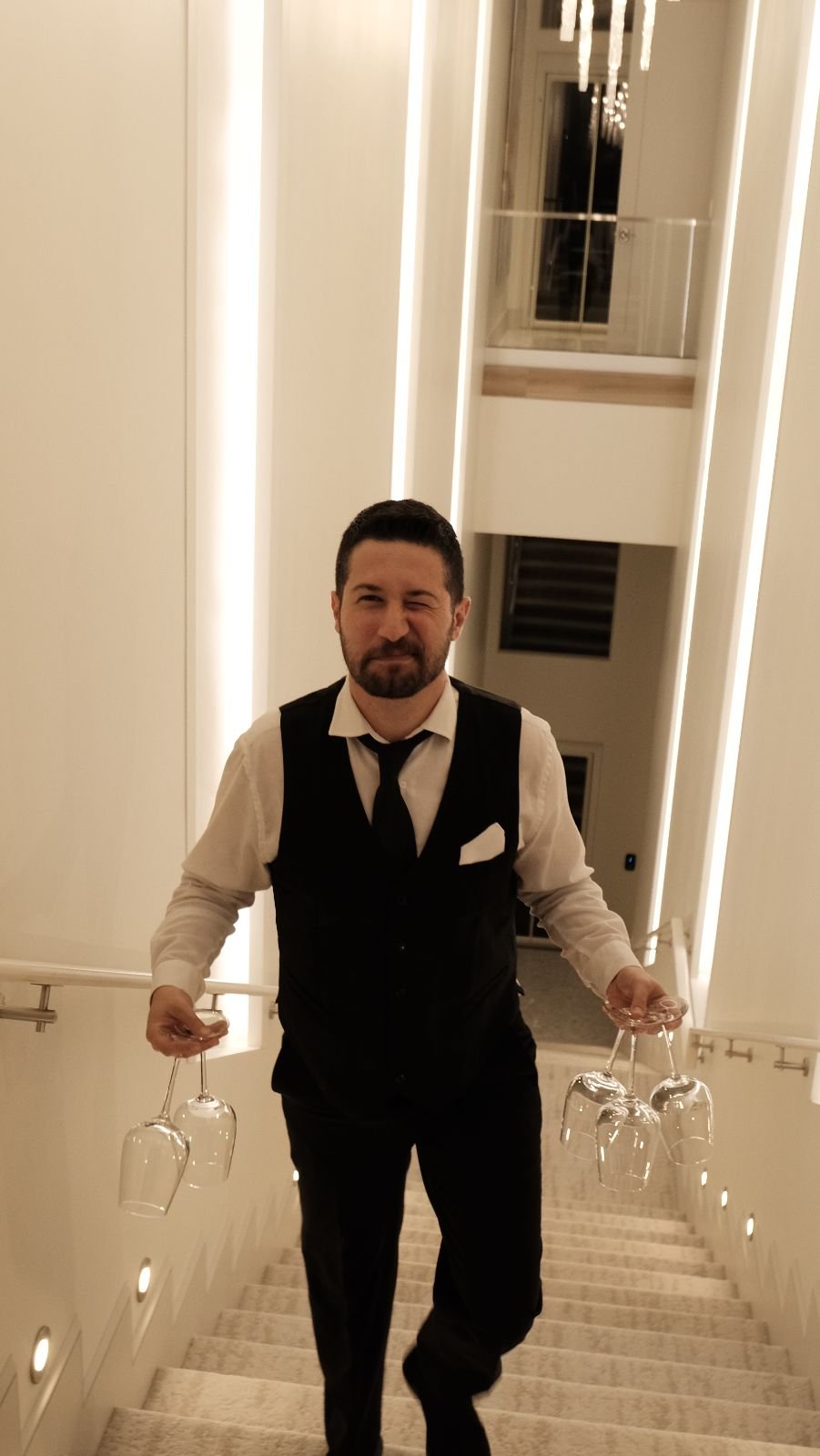 A Bora server in a vest carrying glasses down a staircase