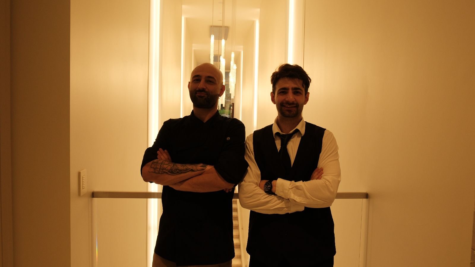 Two members of the Bora team standing with arms crossed in a warmly lit hallway